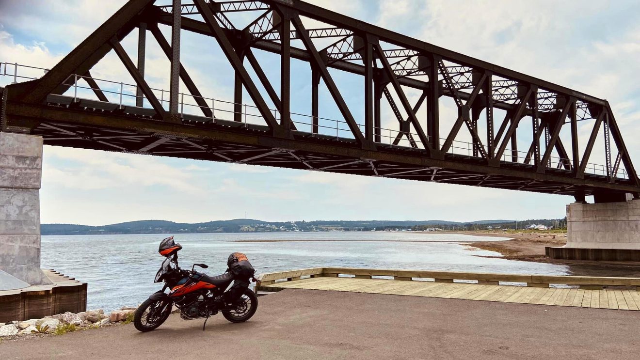Une moto stationnée sous un pont ferroviaire en bord de fleuve