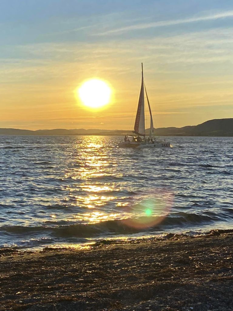 the sun sets behind a sailboat on water in gaspésie