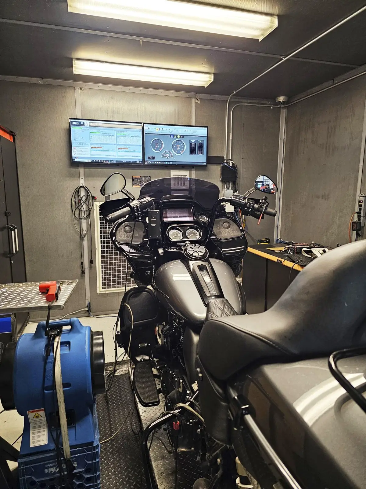 A Harley-Davidson motorcycle being tested in a workshop, with two screens displaying technical data on the dashboard and measuring equipment installed.