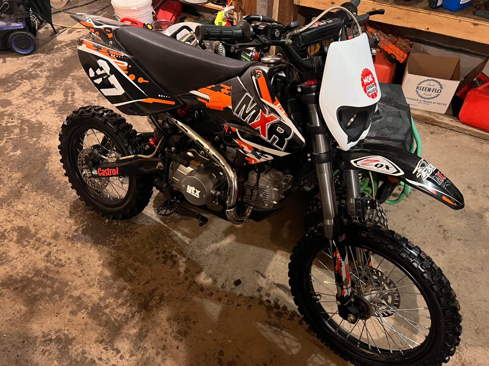 Motocross Apollo MXR 125 noire et orange, idéale pour débutants, garée dans un garage.