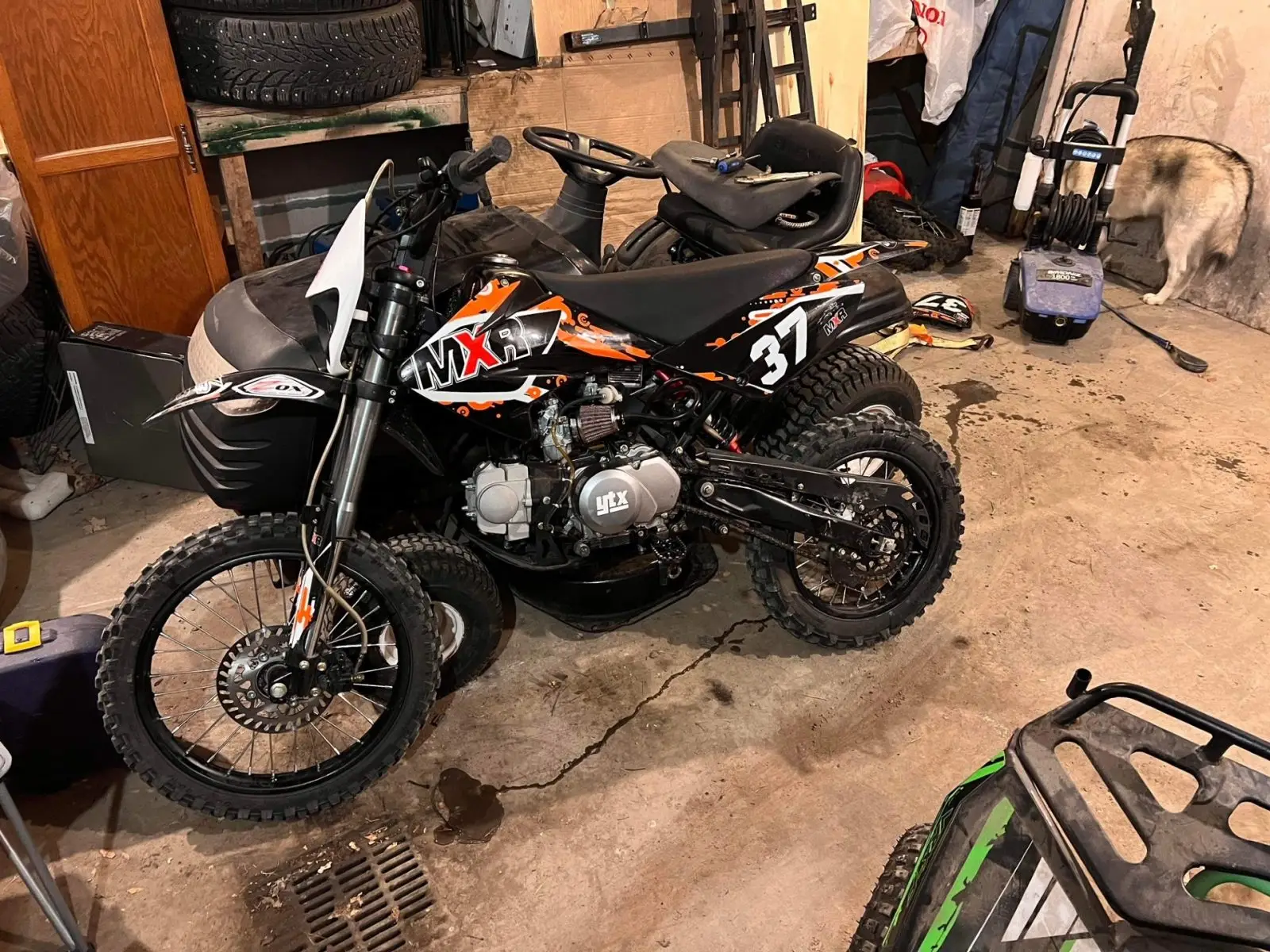 Black and orange Apollo MXR 125 beginner’s motocross bike parked in a tool-filled garage.