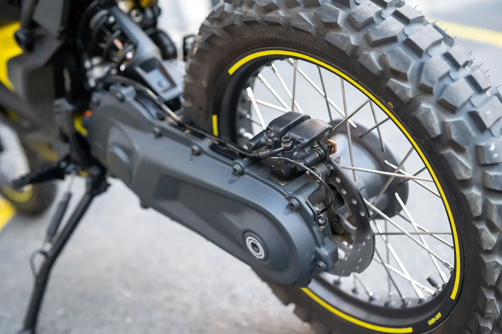 Close-up of the rear wheel and chain case of a Can-Am motorcycle, showing knobby off-road tires and rugged spokes for rough terrain.