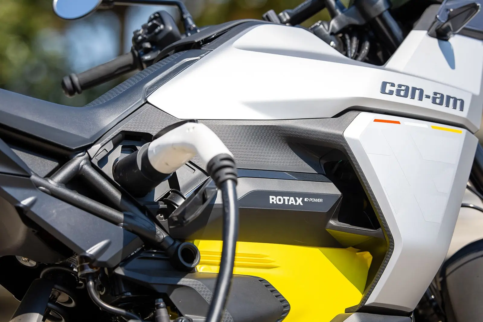 Close-up of a Can-Am electric motorcycle charging, with a cable plugged in on the side.