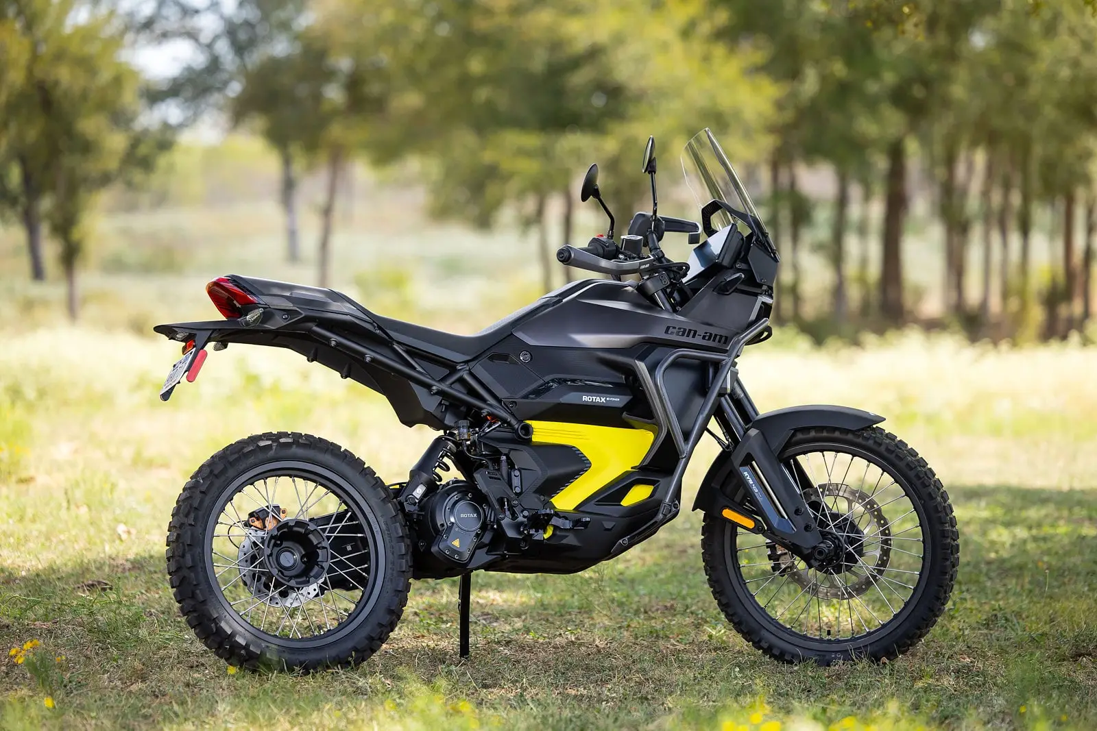 Black and yellow Can-Am Origin electric motorcycle parked on grassy terrain.