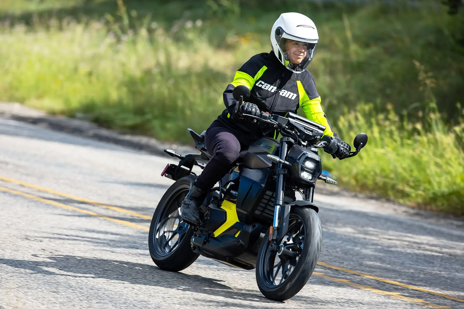 A woman rides a Can-Am Pulse electric motorcycle on a winding road surrounded by greenery.