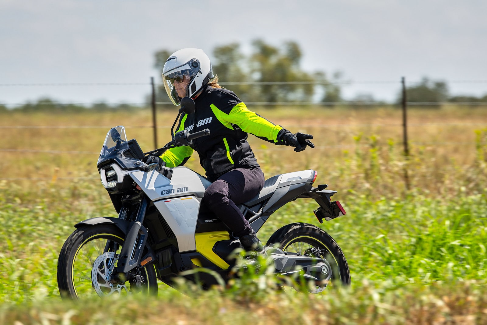 Une personne en moto Can-Am électrique, roulant sur un sentier herbeux, tend le bras vers la droite pour indiquer une direction.