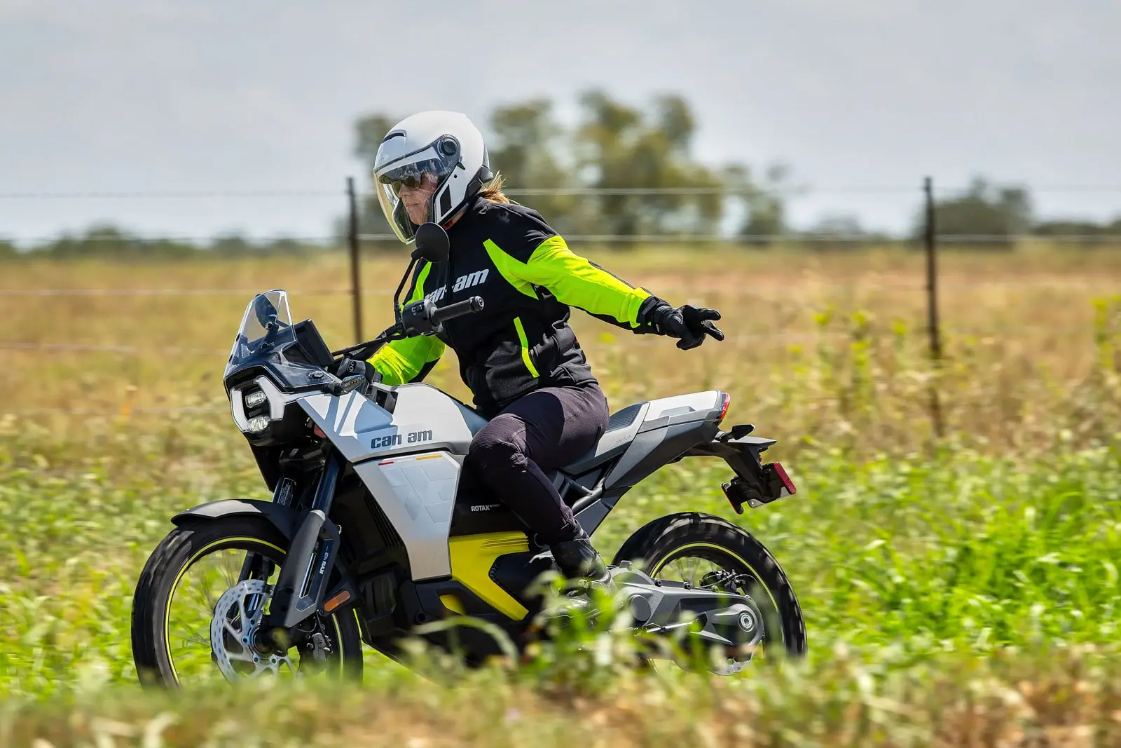 A rider on a Can-Am electric motorcycle on a grassy trail, extending their arm to the right to signal a turn.